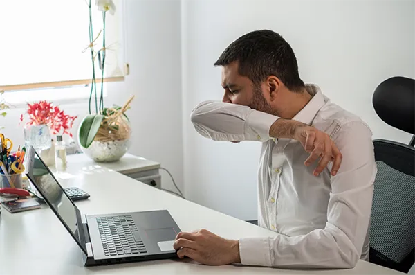 Benefits of Hybrid Working | Person coughing into elbow.