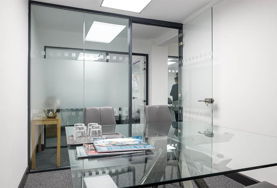 Glass office partitions | Office with glass desk and wall. Newspapers are on the desk as well as some glass cups.