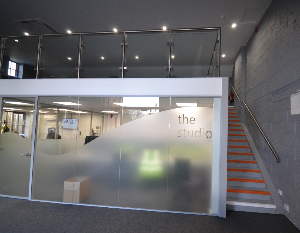 What is a mezzanine floor | Mezzanine floor in a gym setting. Frosted glass window with "the studio" written on it.